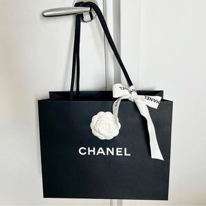 Chanel black paper shopping bag with white flower in center and white ribbon